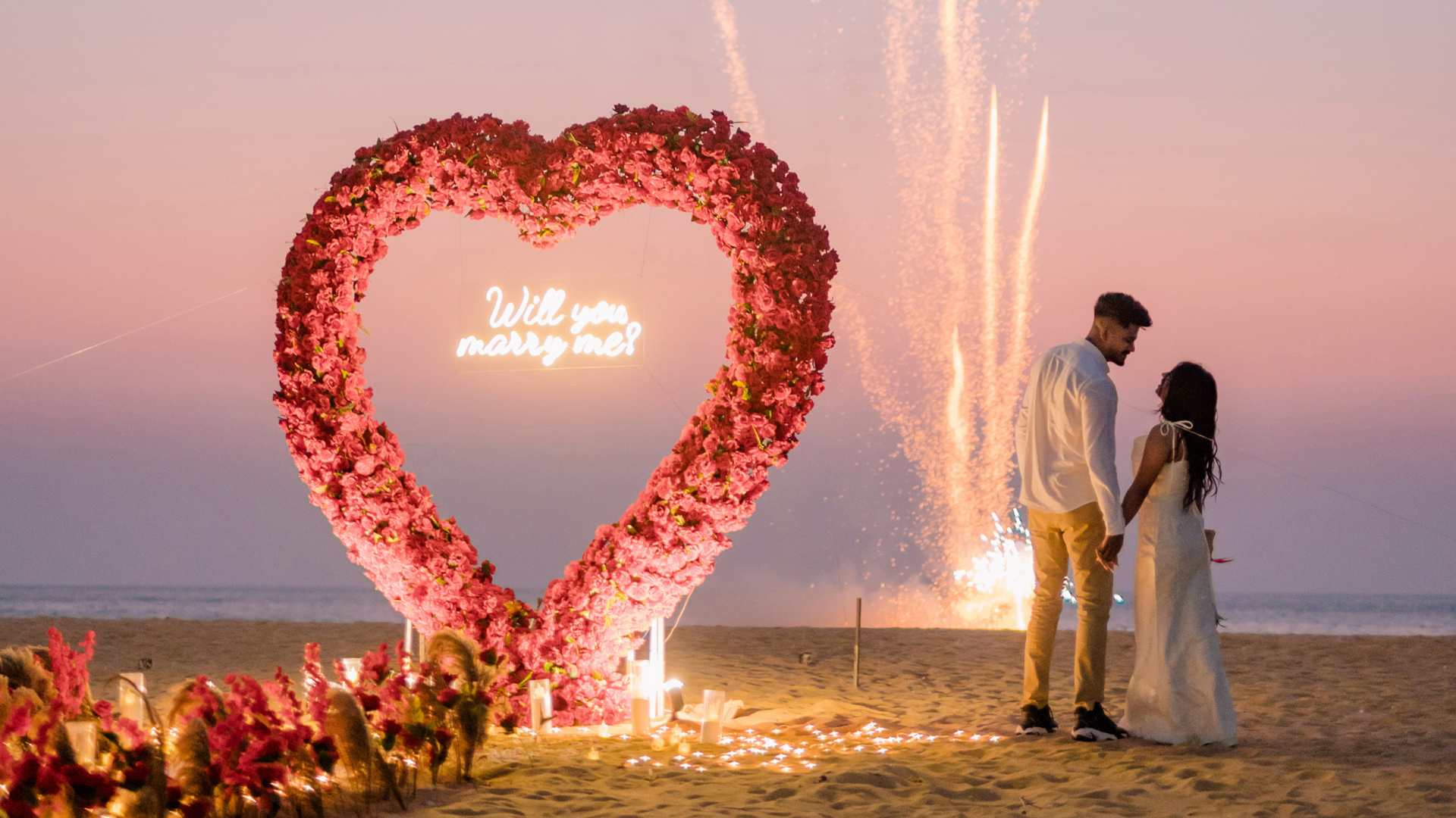 Romantic beach proposal with a heart-shaped flower arch and "Will you marry me?" sign, fireworks in the background, and a couple holding hands, marriage proposal sri lanka, Sri Lankan matrimony, Sri Lanka marriage proposal sites,mangala yojana 2024, matrimony sri lanka, sl marriage proposals, mangala yojana