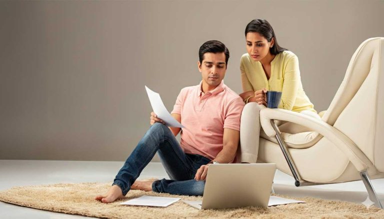A man and woman sitting on the floor with a laptop.