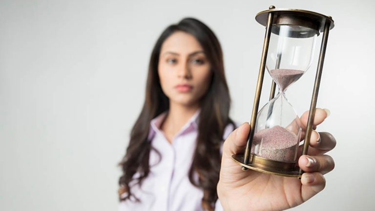 A woman holding an hourglass filled with sand, symbolizing time, patience, and important life decisions such as marriage.